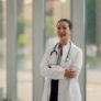 Confident female doctor smiling with crossed arms in hospital corridor